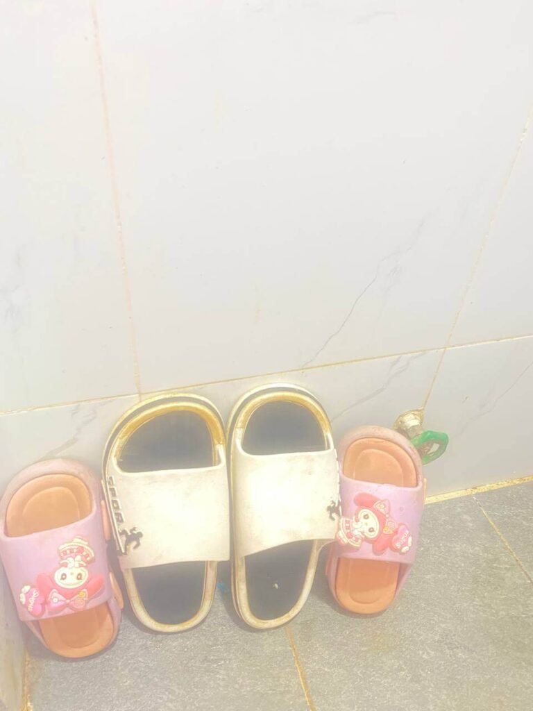 Two pairs of wet children's sandals leaning against a tiled bathroom wall to dry