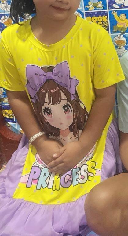 A young girl wearing a bright yellow shirt with an anime character and the word Princess on it.