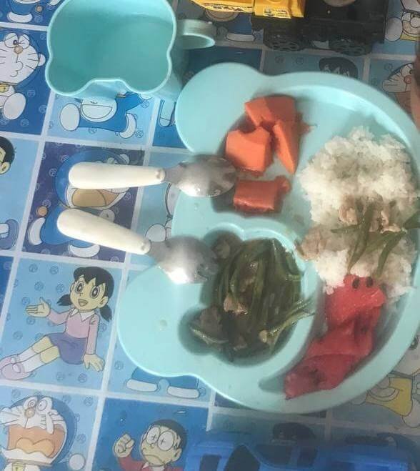 A light blue children's partitioned plate with rice, green beans, and freshly cut fruit.