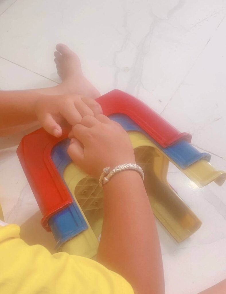 A child's hands trying to pull apart tightly stacked red, blue, and yellow plastic step-stools.