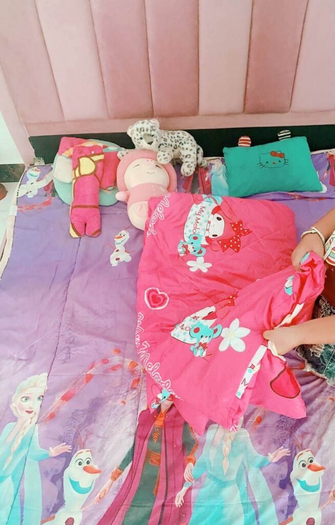 A child's hands pulling up a bright pink character blanket to make their bed in the morning.