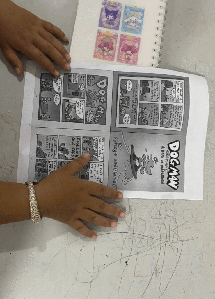 A child's hands holding open a black-and-white printed page of a Dog Man comic book on a table.
