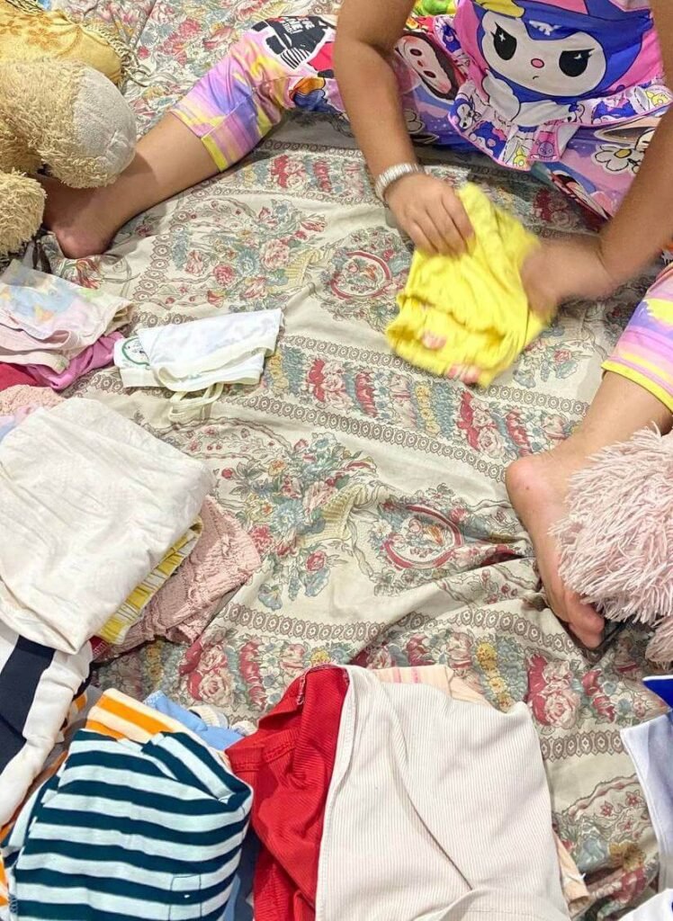 An eight-year-old child sitting on a bed, actively sorting and folding colorful clean laundry into separate piles.