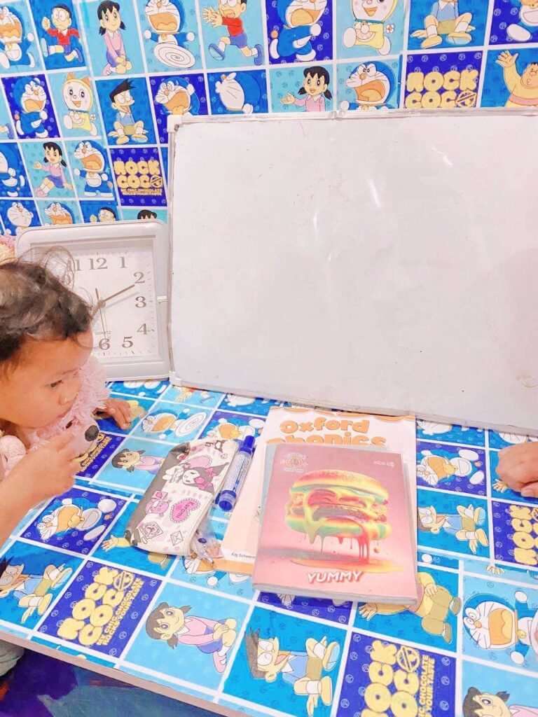 A child's colorful study table featuring a whiteboard, clock, and the infamous pen case next to school books.