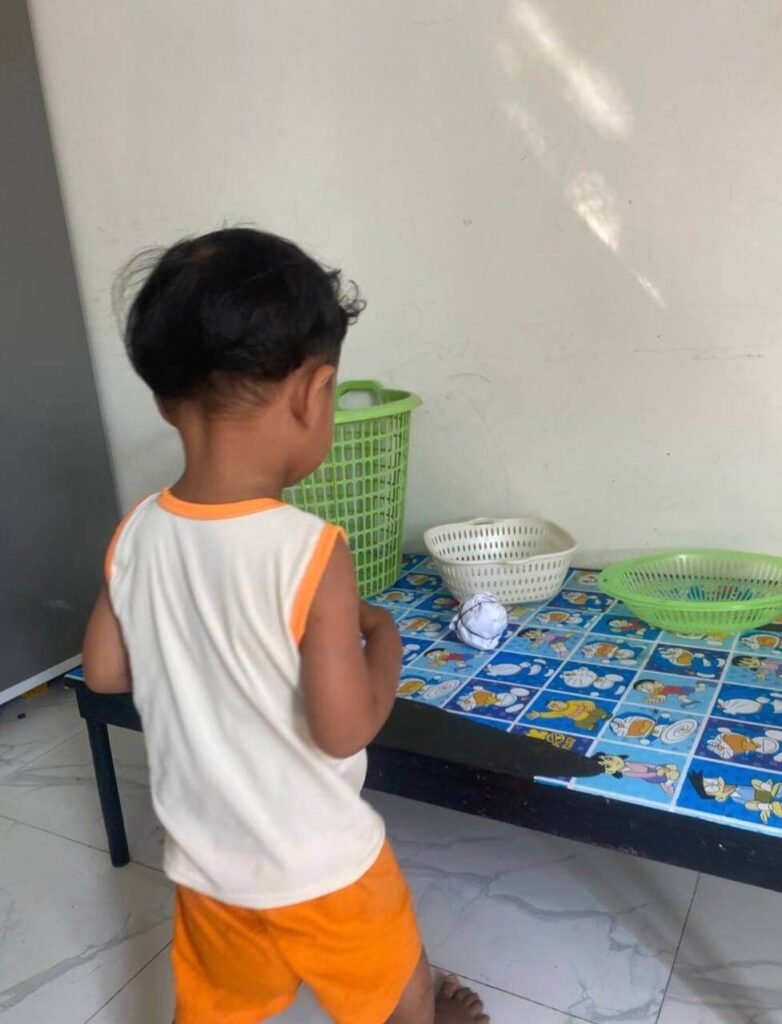 A young boy aiming a crumpled ball of paper at a collection of plastic laundry baskets and small bowls.