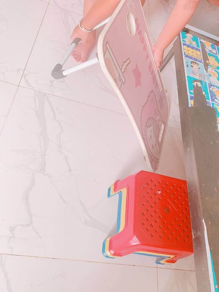 A child's hands moving a small pink foldable table and a red plastic stool to set up for mealtime.