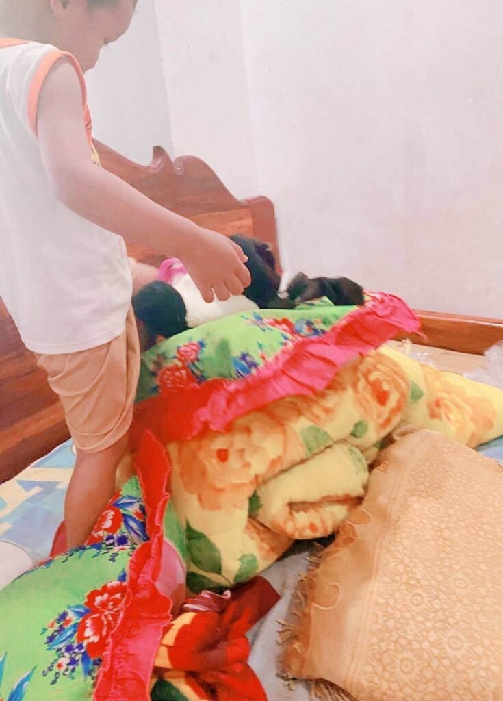 A young boy climbing over a large pile of colorful folded blankets and pillows.