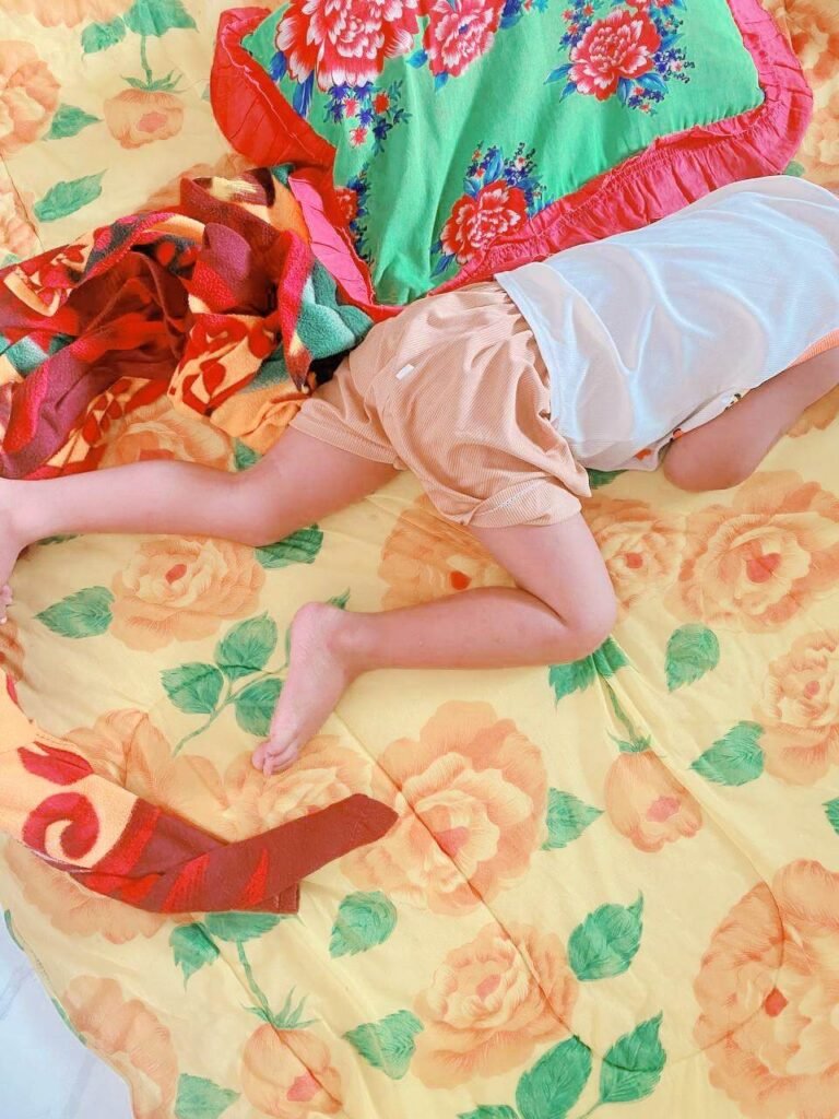 A young boy lying flat and rolling across a bright yellow floral blanket on the floor.