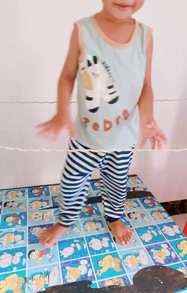 A young boy in striped pants carefully stepping over a piece of string stretched horizontally across the room.