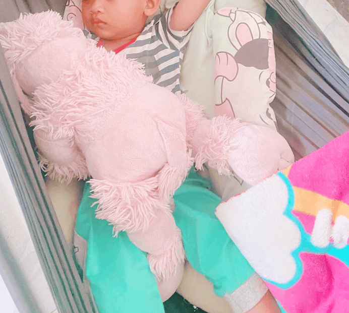 A toddler sleeping soundly in a hammock while holding a large pink stuffed animal.