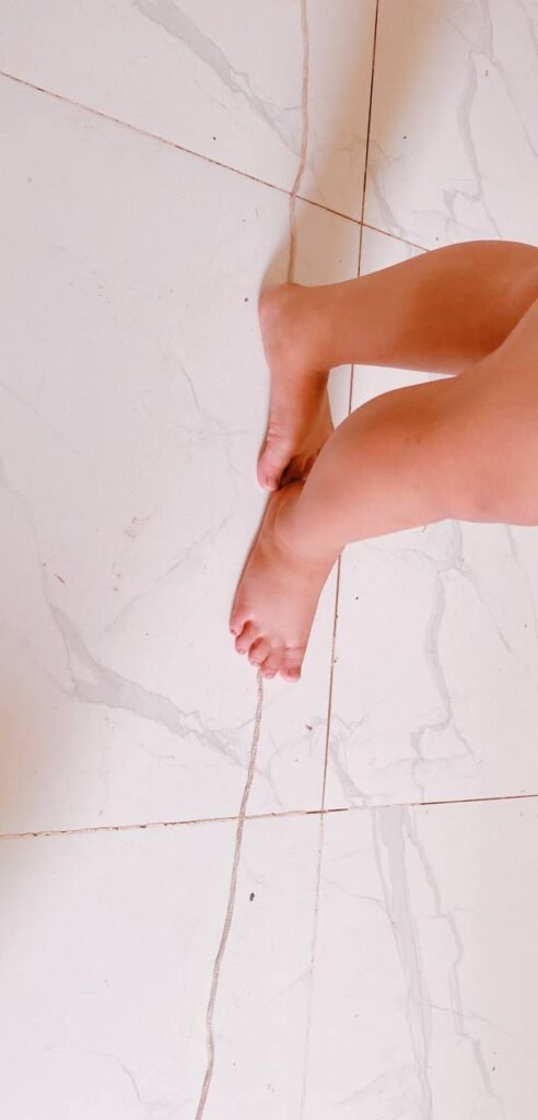 A close-up of a child's bare feet balancing carefully on a thin string line taped across a white tile floor.