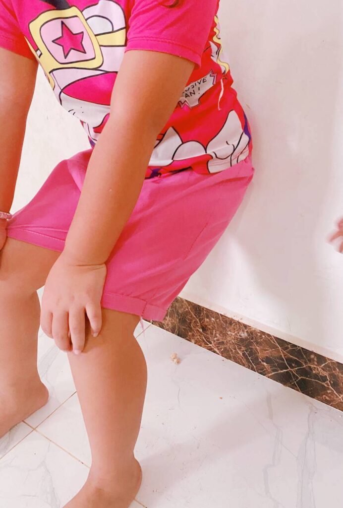 A close-up of a child's legs bent at a 90-degree angle, performing a wall sit exercise against a plain white wall.