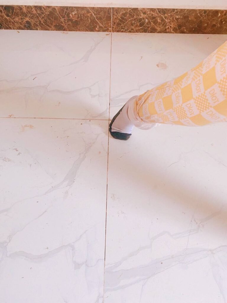 A close-up of a child's foot wearing a patterned sock, stepping on a smooth white tile floor.
