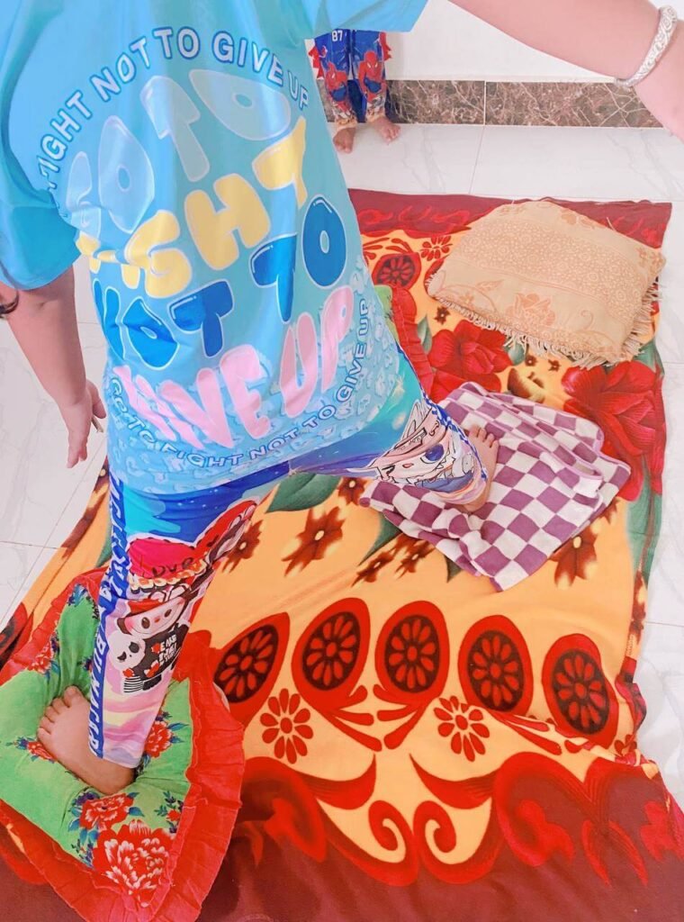 A child stepping carefully onto a folded towel and a pillow placed on top of a colorful floral blanket on the floor.