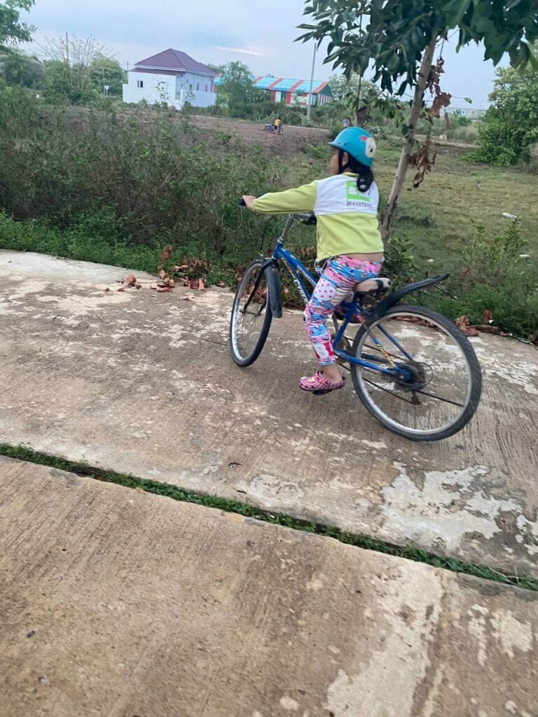 A young girl wearing a blue helmet safely rides a bicycle down a concrete path outdoors.