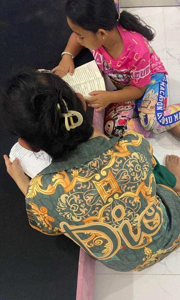 An overhead view of a mother and daughter sitting close together on the floor reading a book out loud.