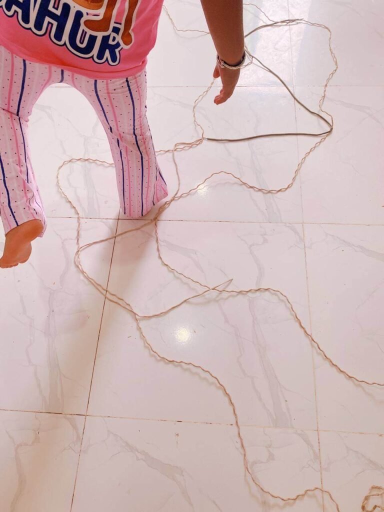 A child's bare feet carefully stepping between pieces of string laid out in a winding, wavy pattern on a white tile floor.