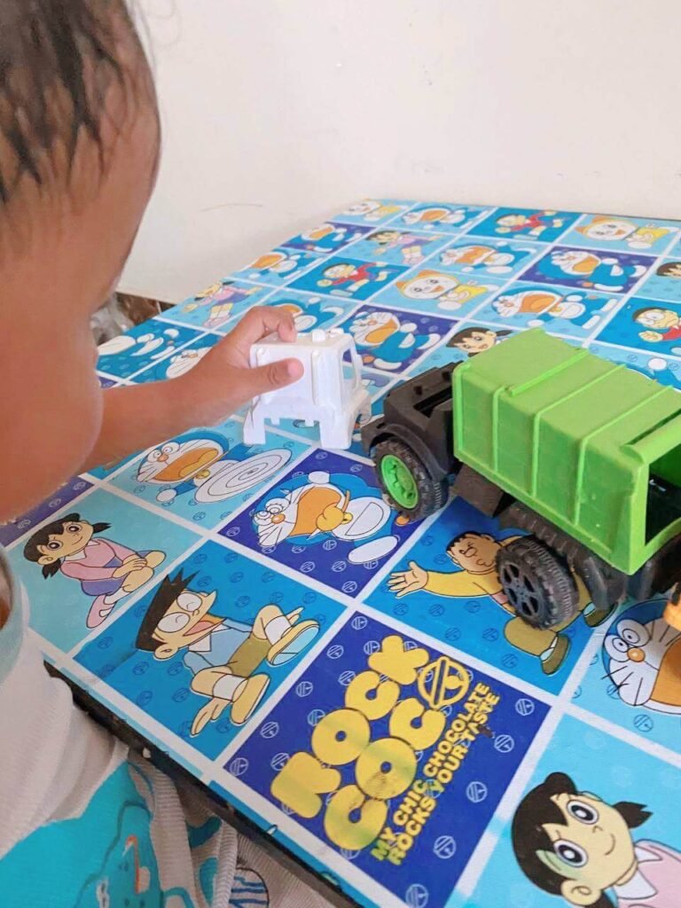 A young child playing with a green toy truck and a white toy car on a Doraemon table.