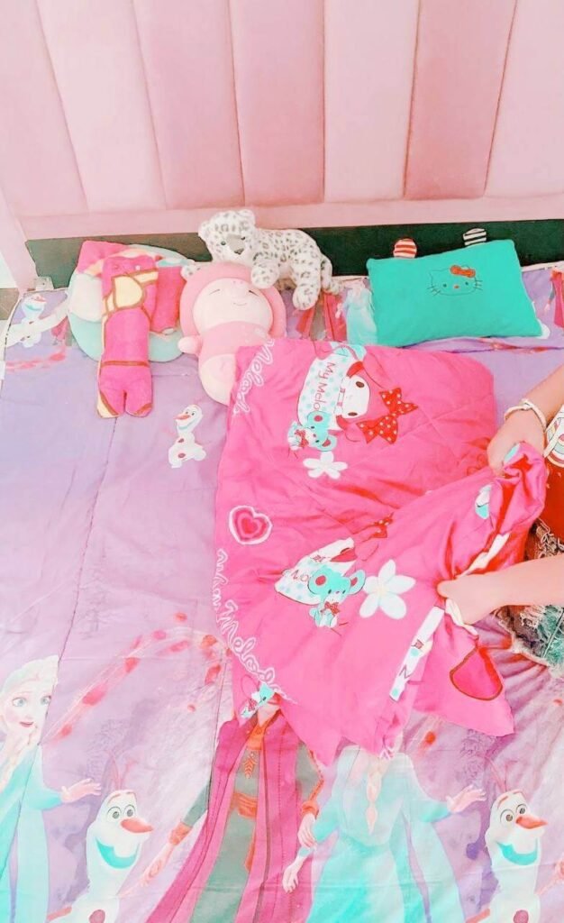 A close-up shot of a child's hands pulling a bright pink blanket over bedding featuring Frozen and Olaf characters.