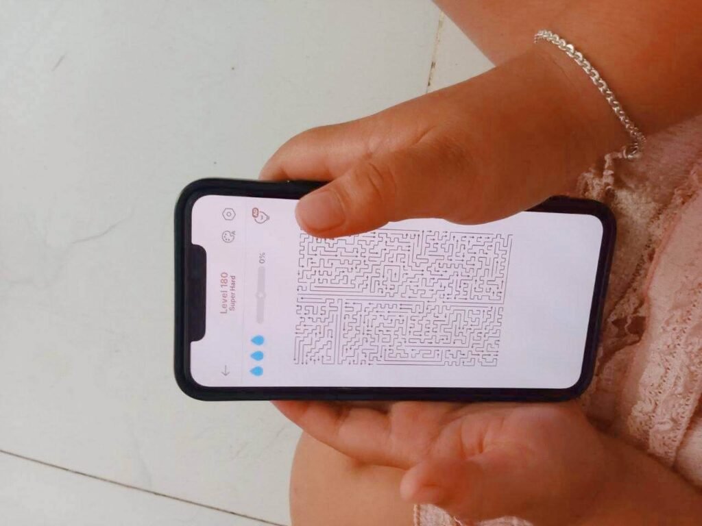 Close up of a child's hands holding a smartphone displaying a complex digital maze game at Level 180, labeled Super Hard.