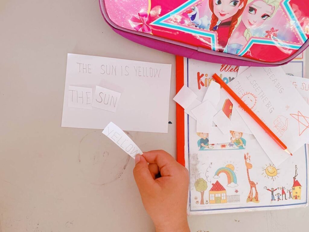 Hand-cut paper word strips being used for a cut and paste sentence building activity on a table.