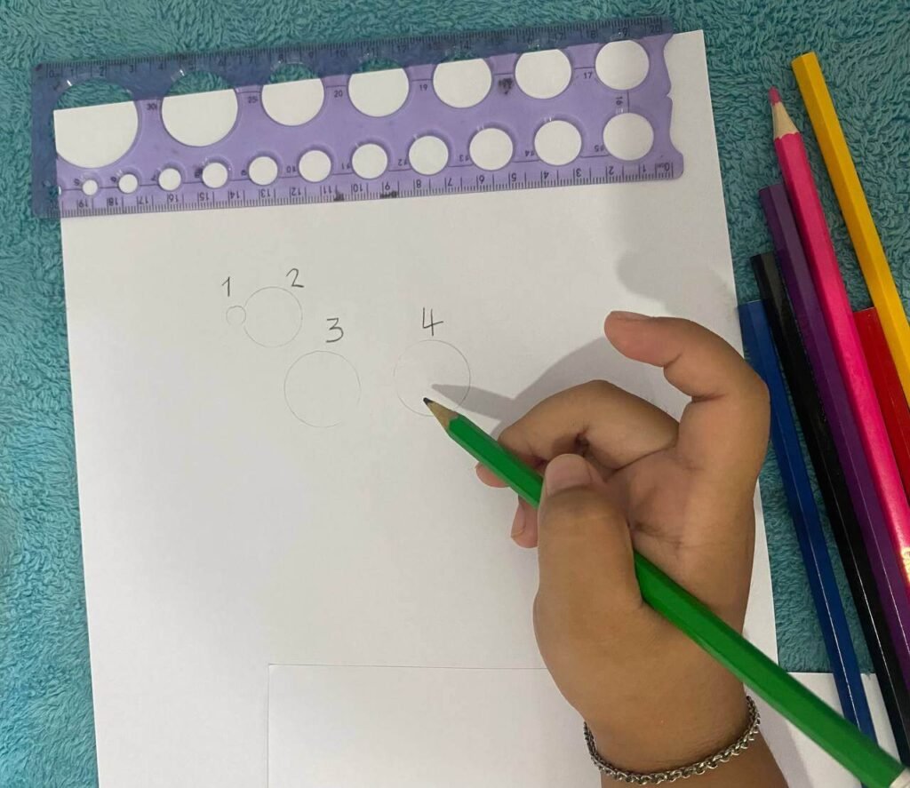 A child holding a green pencil with a relaxed whisper grip in the middle of the barrel, drawing four numbered guide circles for a dog's body.