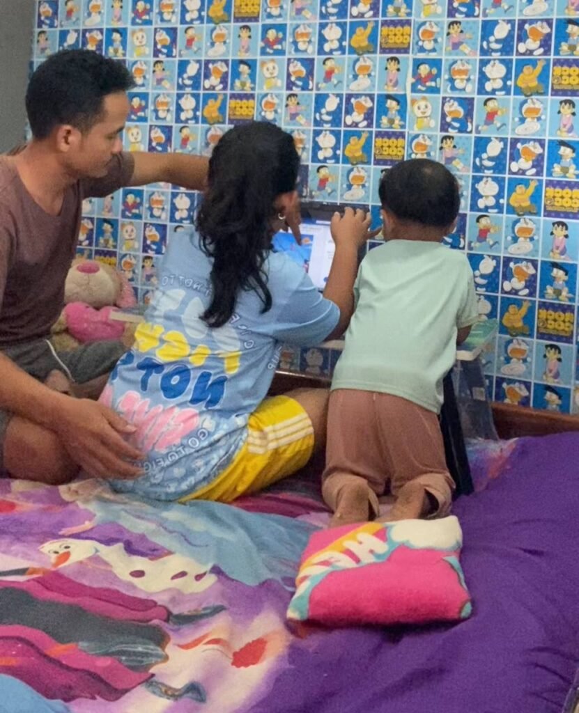 A father sitting on a bed with two young children who are focused on a laptop screen to solve a problem.