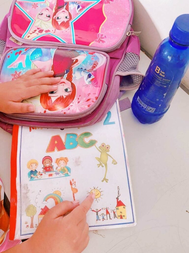 A kindergartner pointing to a picture of a sun on their textbook cover, used to create familiar sight word sentences.