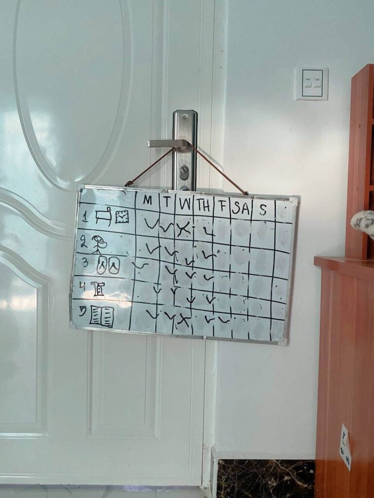 The completed child-drawn whiteboard morning checklist with handwritten checkmarks, tied and hanging directly from a silver bedroom door handle.