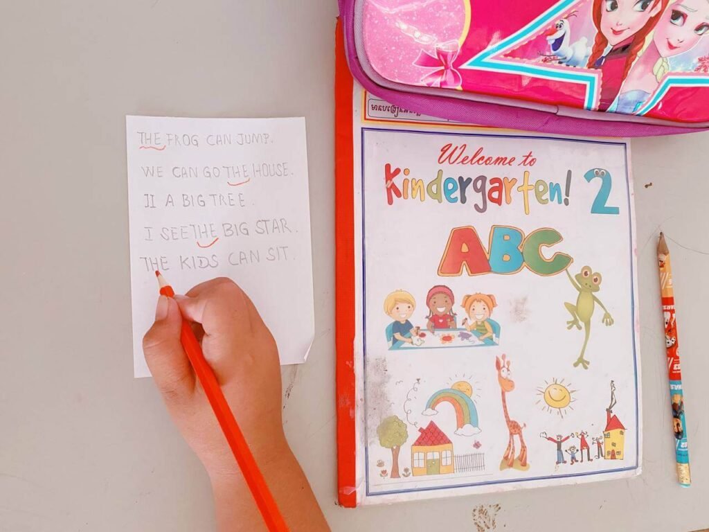 A child using a red pencil to hunt and underline the target sight word 'the' in a list of handwritten sentences.