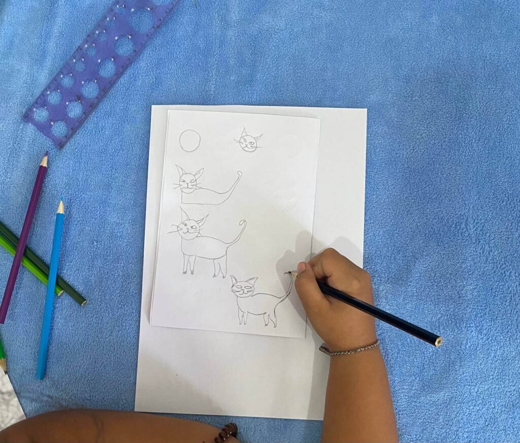 Drawing tutorial steps for a walking cat, illustrating a child using a black pencil to add a long tail and legs to a circle-based cat sketch.
