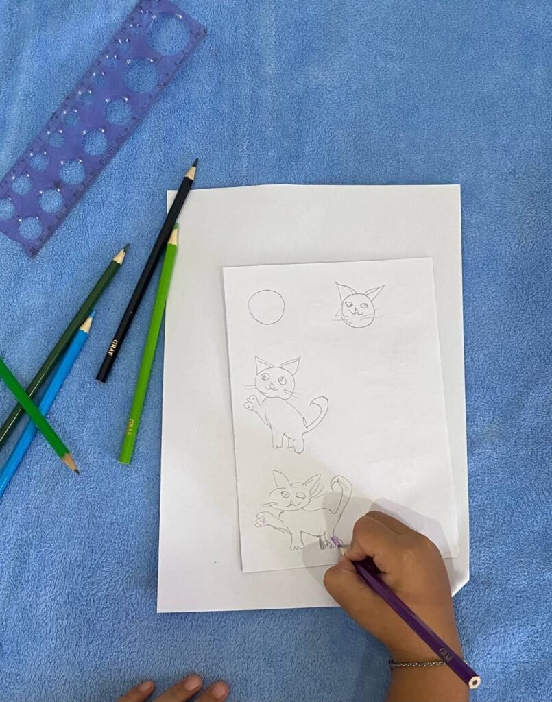 A young girl coloring the raised paw of a waving cat drawing with a purple pencil, demonstrating a fun and easy cat pose for kids.