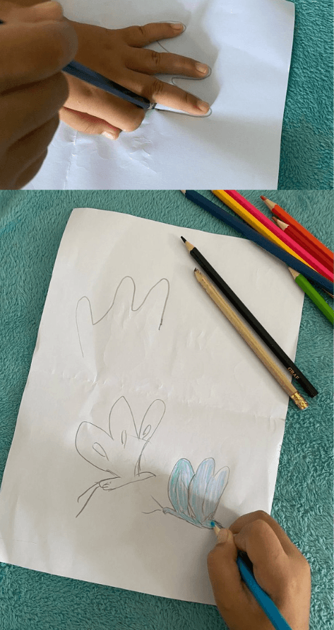 A kid tracing three fingers with a pencil and coloring smaller baby butterfly wings with a blue colored pencil.