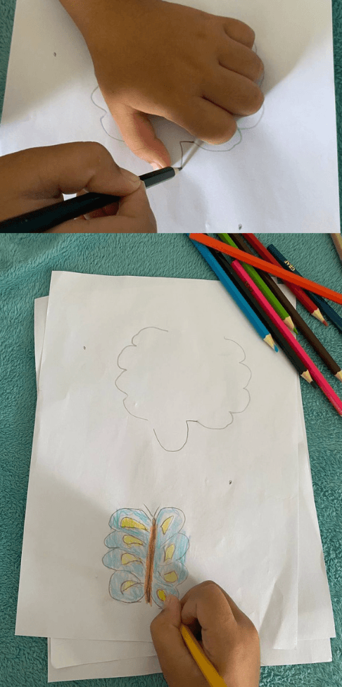 A child tracing around a closed fist with a black pencil to create a textured back-view butterfly drawing.