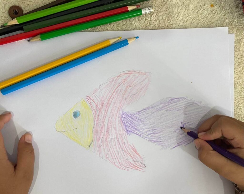 A child using a purple colored pencil to shade the tail of a fish drawing that was traced from a leaf.