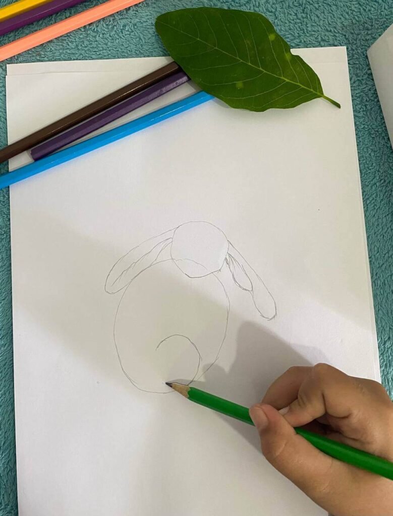 A child sketching a backward letter C on the lower back of a drawn bunny to create the shape of folded hind legs.