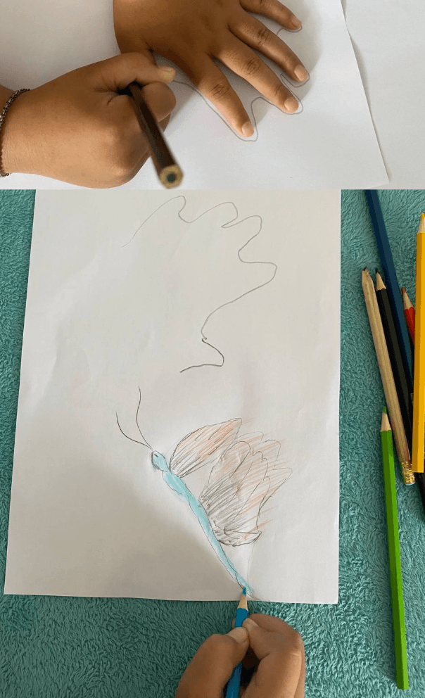 A child tracing their open hand with five fingers spread out on white paper to draw a flying butterfly template.